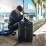 a man holding his head near a suitcase, in an airport