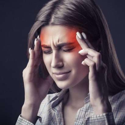 a woman holding her temples, the color of the photo is largely unsaturated save for some red glowing spots on her head